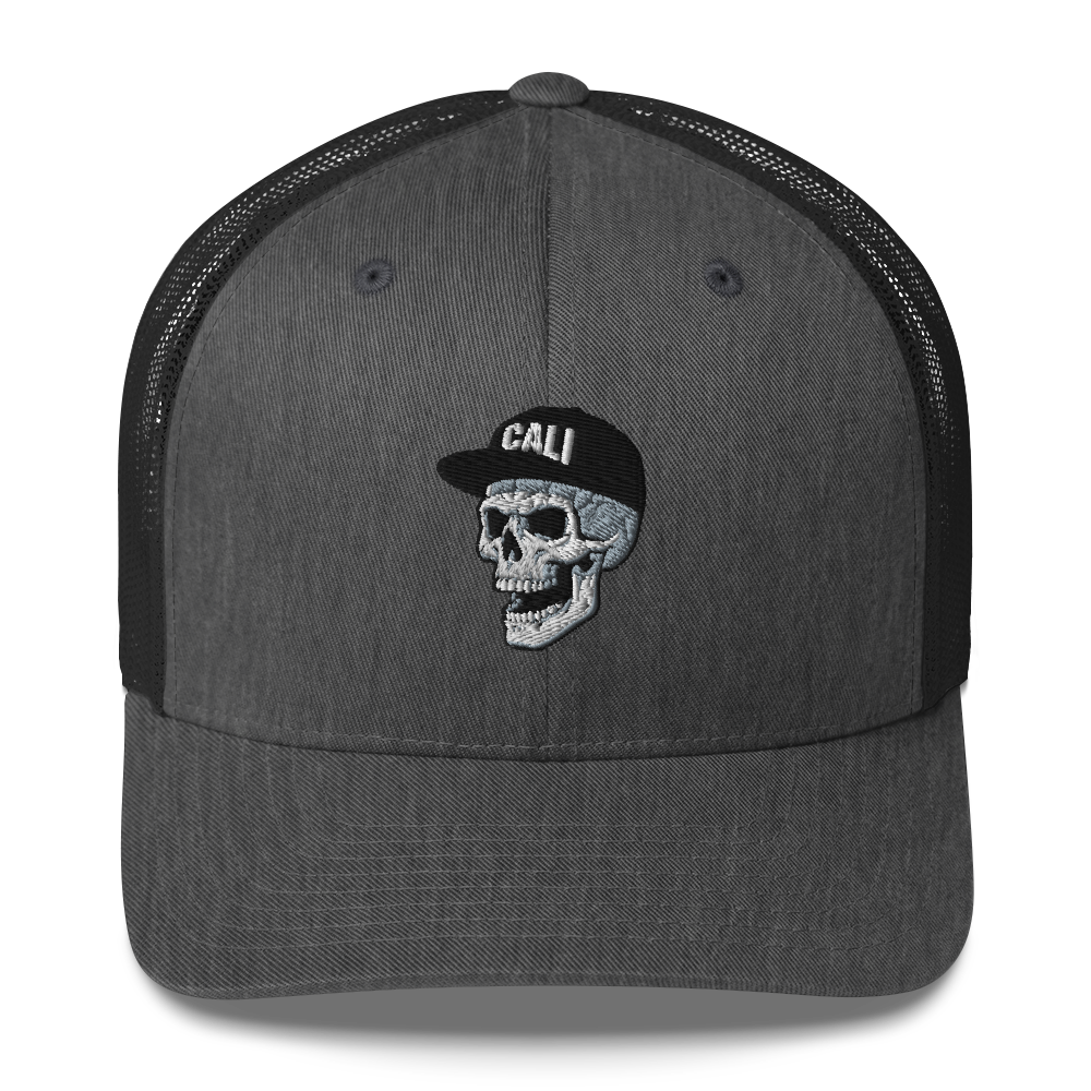 A dark gray trucker hat with black mesh back panels and a central embroidered skull wearing a black cap with the word 'CALI' in white.