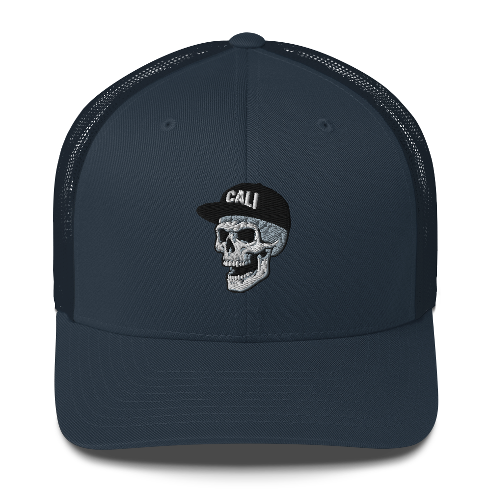 A navy blue trucker hat with a black mesh back and a front embroidered patch featuring a white and black skull wearing a cap with the word 'CALI'.