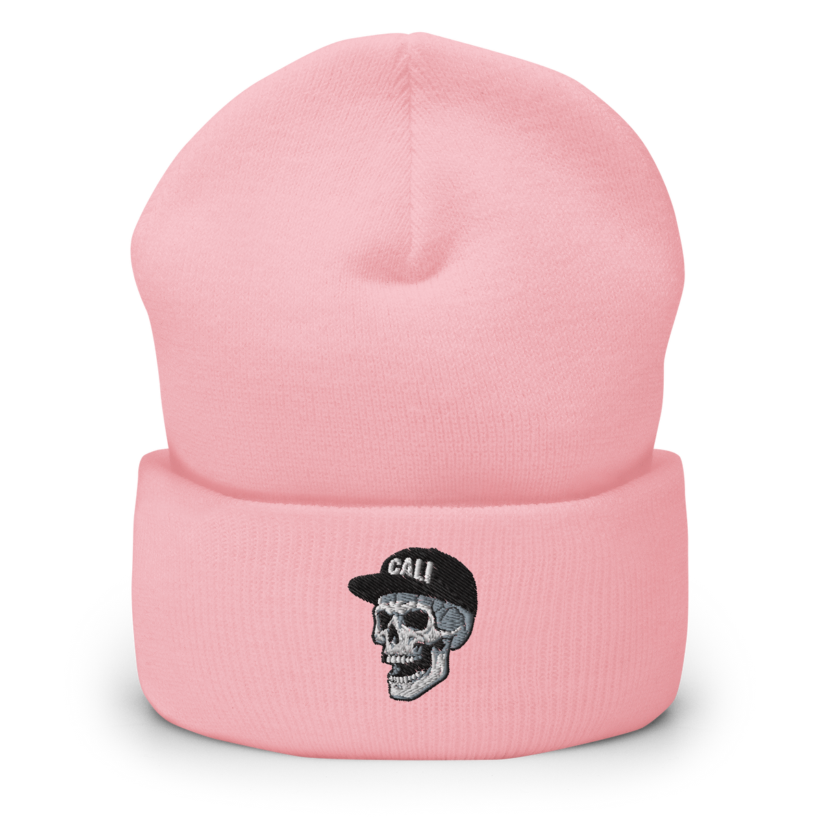 A light pink knit beanie hat with a folded cuff, featuring an embroidered graphic of a gray and black skull wearing a black cap with the word 'CALI' in white.