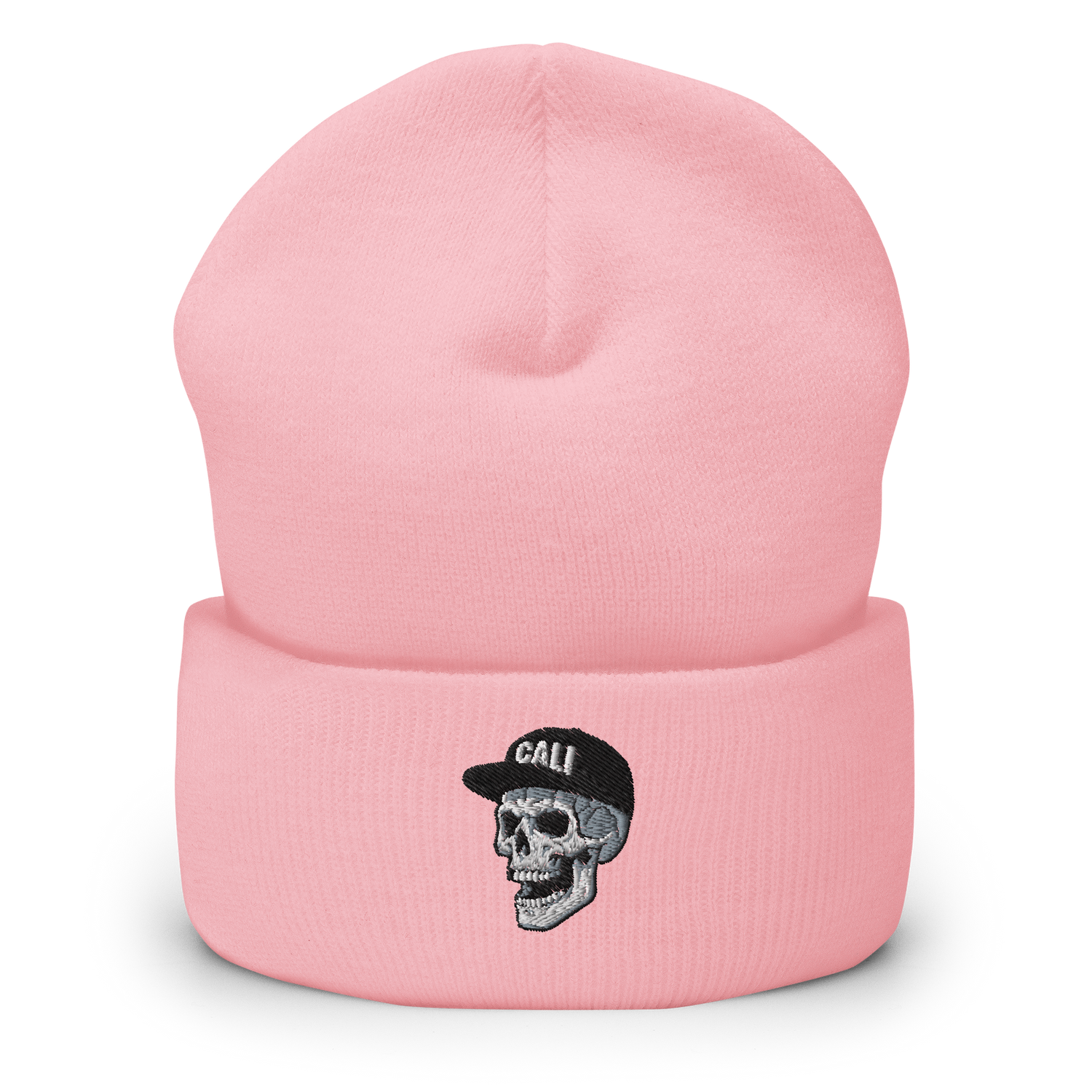 A light pink knit beanie hat with a folded cuff, featuring an embroidered graphic of a gray and black skull wearing a black cap with the word 'CALI' in white.