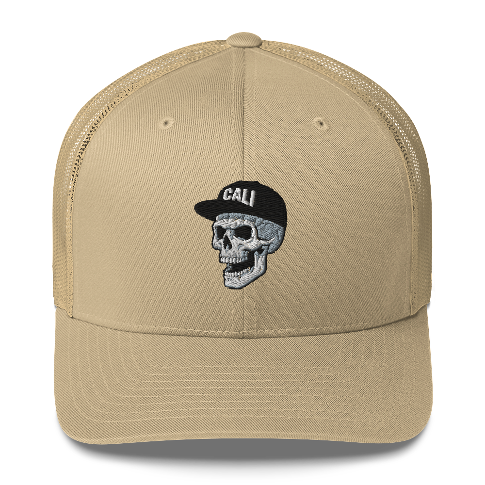 A tan trucker-style cap with a black mesh back and a central embroidered graphic of a skull wearing a black cap with the word 'CALI' in white.