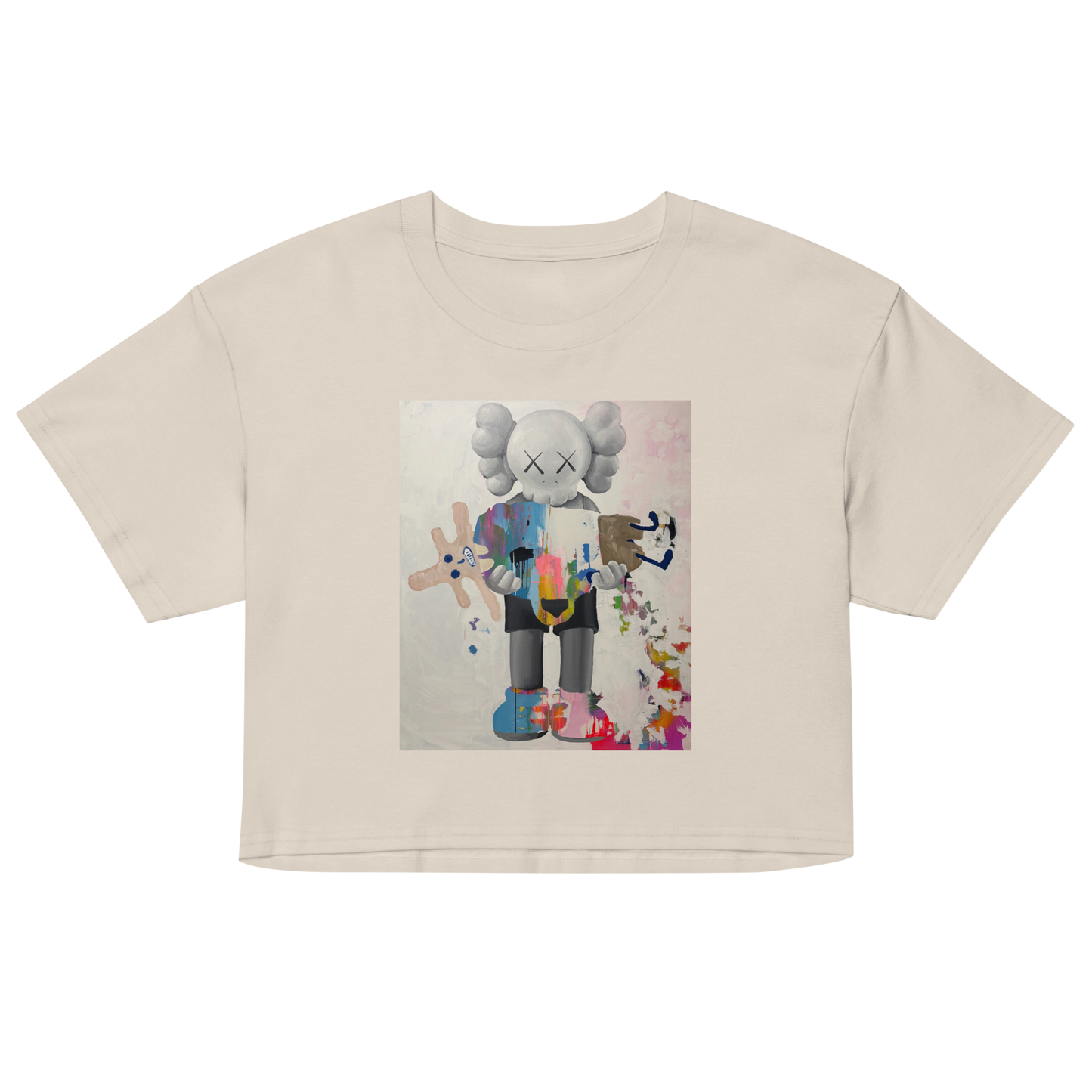 A beige short-sleeve crop top t-shirt featuring a colorful graphic print of a stylized cartoon character resembling KAWS, Daniel Maltzman artist.