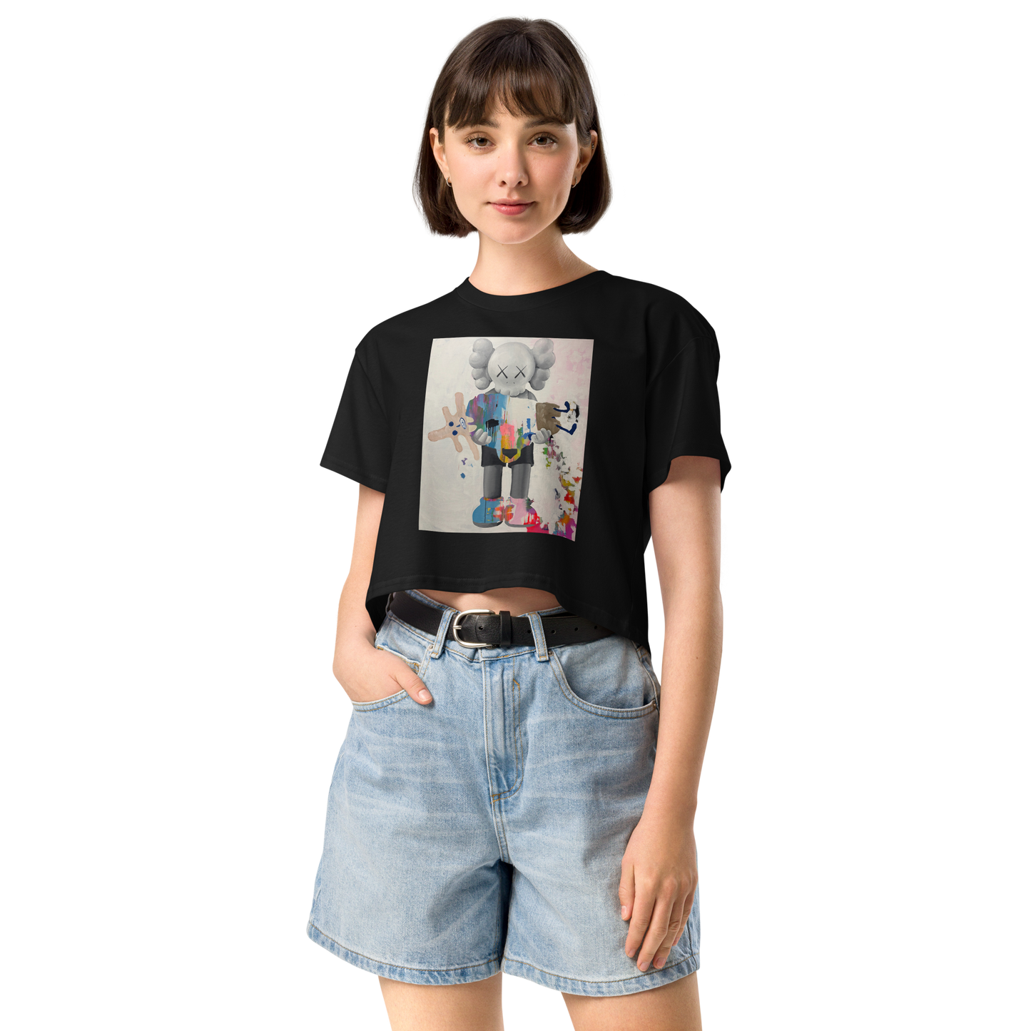 A woman modeling a black crop top t-shirt with a colorful graphic print of a cartoon character, paired with light-wash denim shorts. Daniel Maltzman artist. 