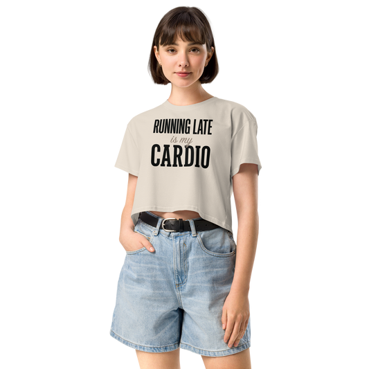 A woman modeling a light beige cropped t-shirt with the black printed text 'RUNNING LATE is my CARDIO' paired with light blue denim shorts.
