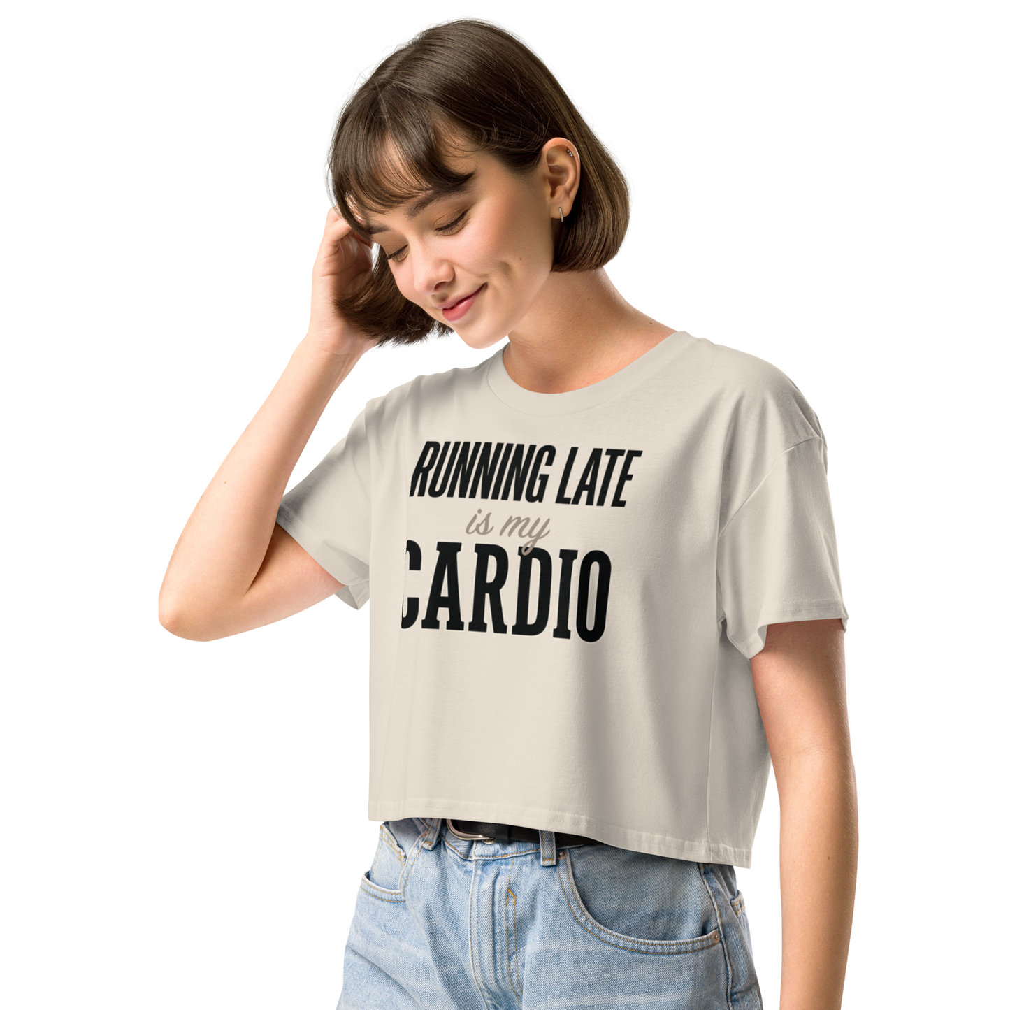 A woman wearing a light beige cropped t-shirt with the black printed text 'RUNNING LATE is my CARDIO' and light blue jeans.