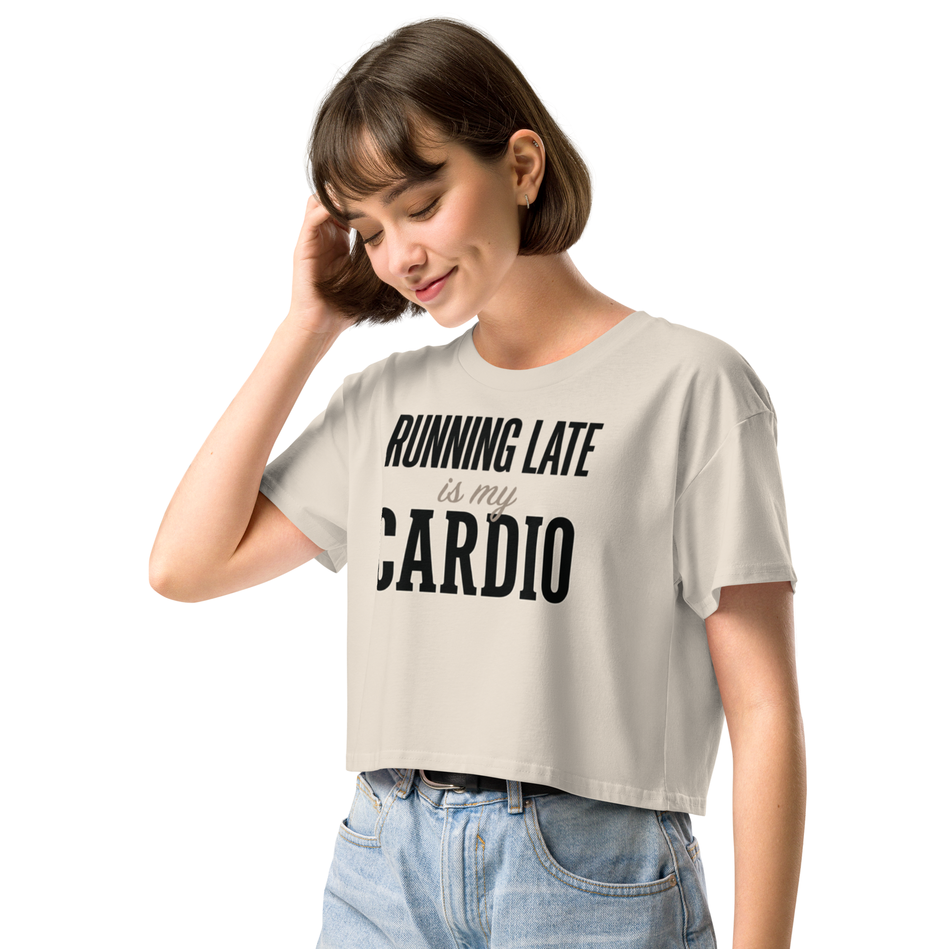 A woman wearing a light beige cropped t-shirt with the black printed text 'RUNNING LATE is my CARDIO' and light blue jeans.
