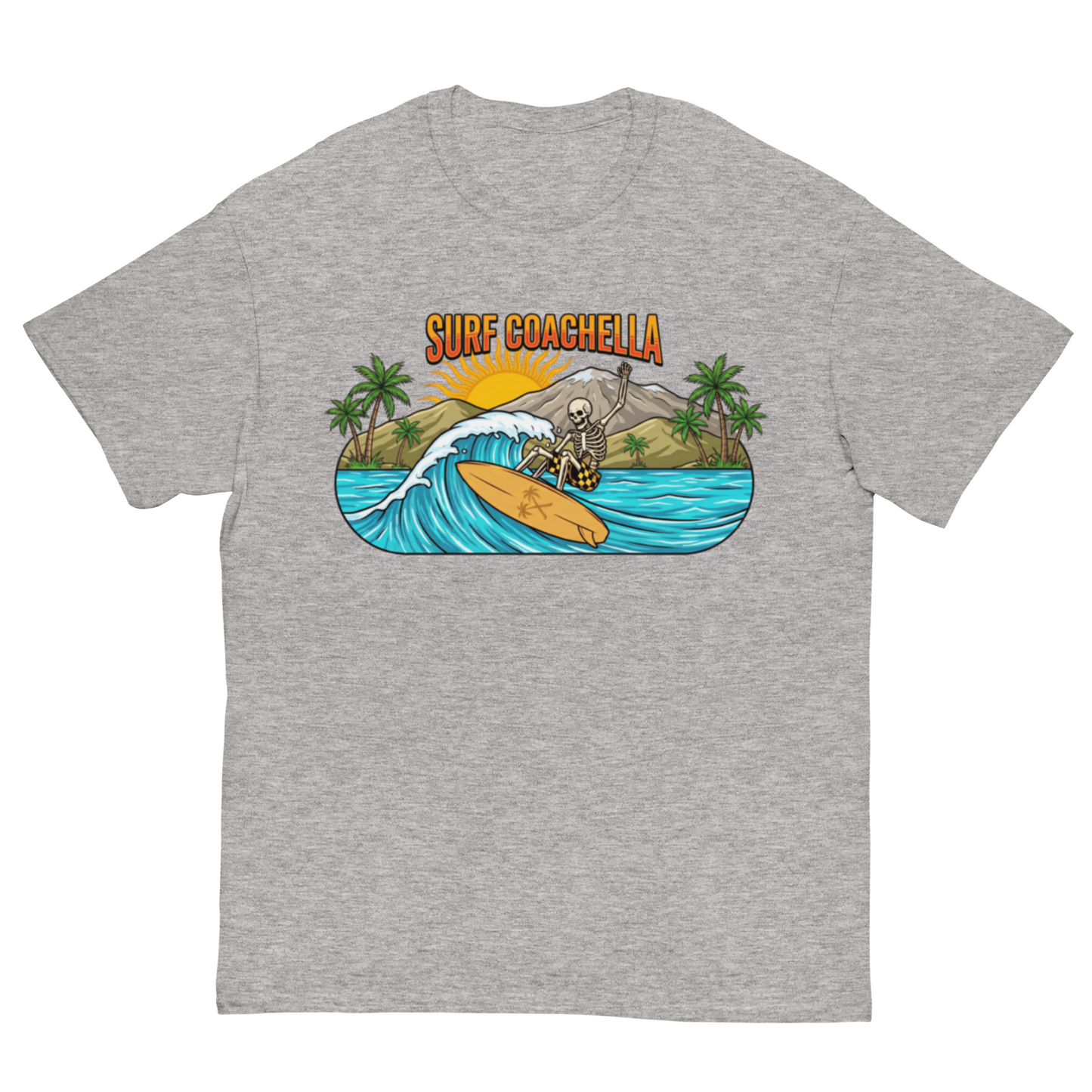 A heather gray short-sleeve crewneck t-shirt featuring a colorful graphic print on the chest. The graphic shows a skeleton surfer riding a wave on a yellow surfboard, with palm trees, a mountain, and the text 'SURF COACHELLA' in orange above it.