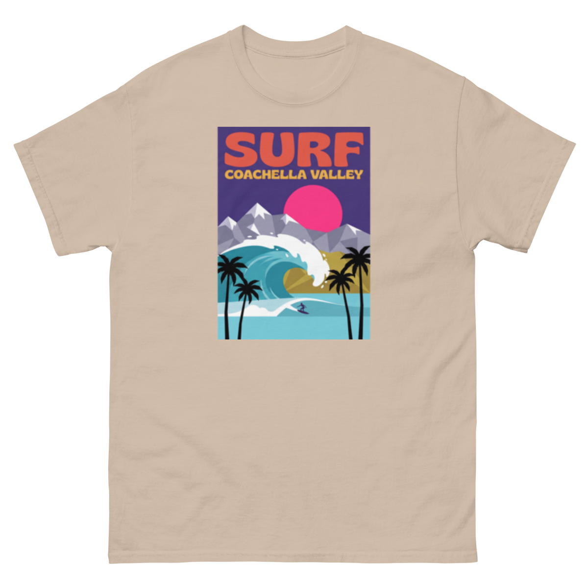 A beige crewneck t-shirt featuring a colorful graphic print on the front with the text 'SURF COACHELLA VALLEY' and an illustration of a surfer, palm trees, mountains, and a pink sun.