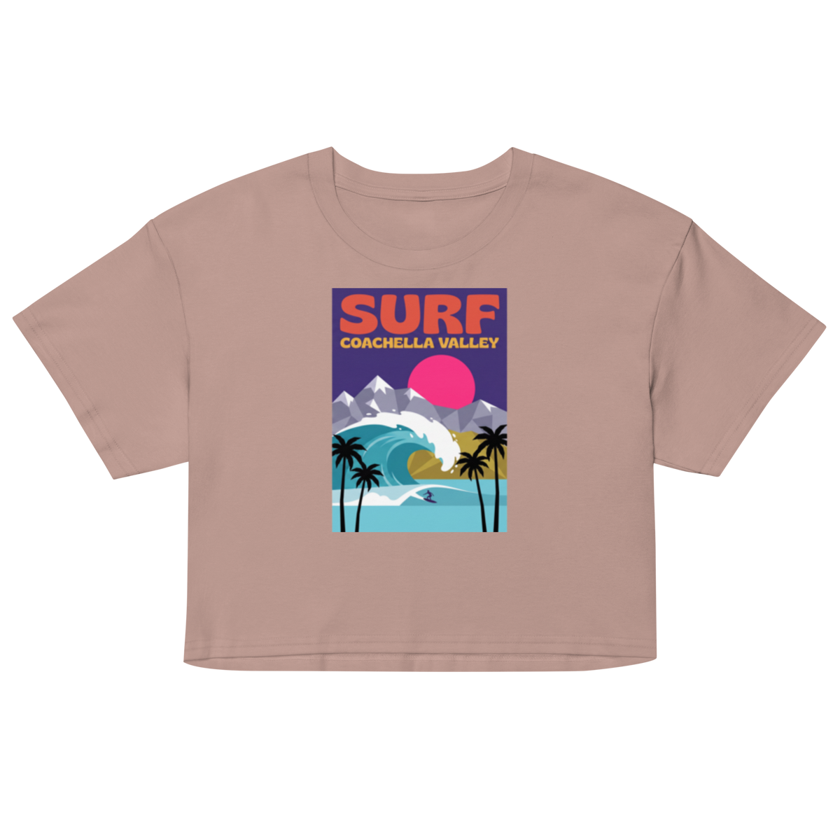 A cropped short-sleeve t-shirt in a dusty rose or mauve color, featuring a colorful graphic print on the front with the text 'SURF COACHELLA VALLEY' and an illustration of a wave, mountains, and palm trees.