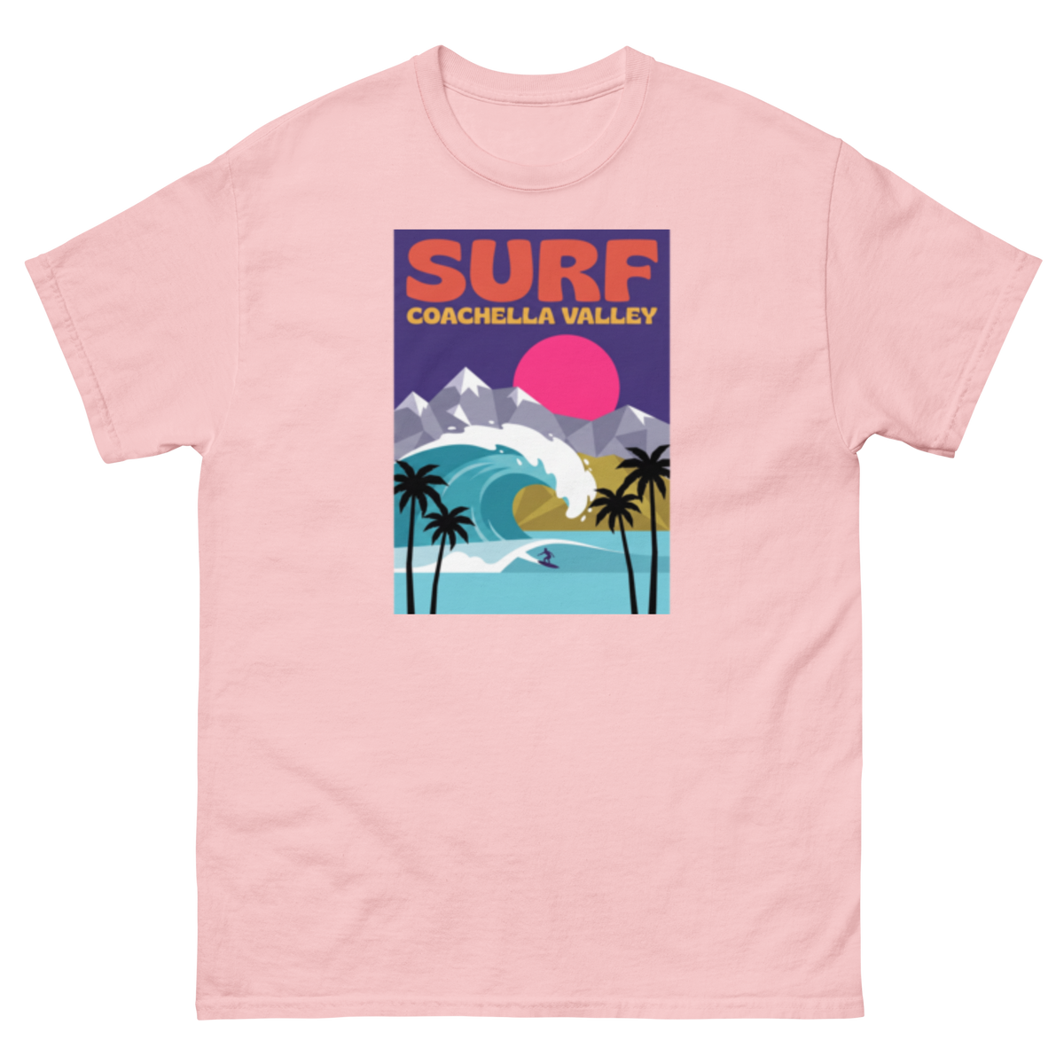 A light pink short-sleeve crewneck t-shirt featuring a colorful graphic print on the front with the text 'SURF COACHELLA VALLEY' and an illustration of a wave, mountains, palm trees, and a pink sun.