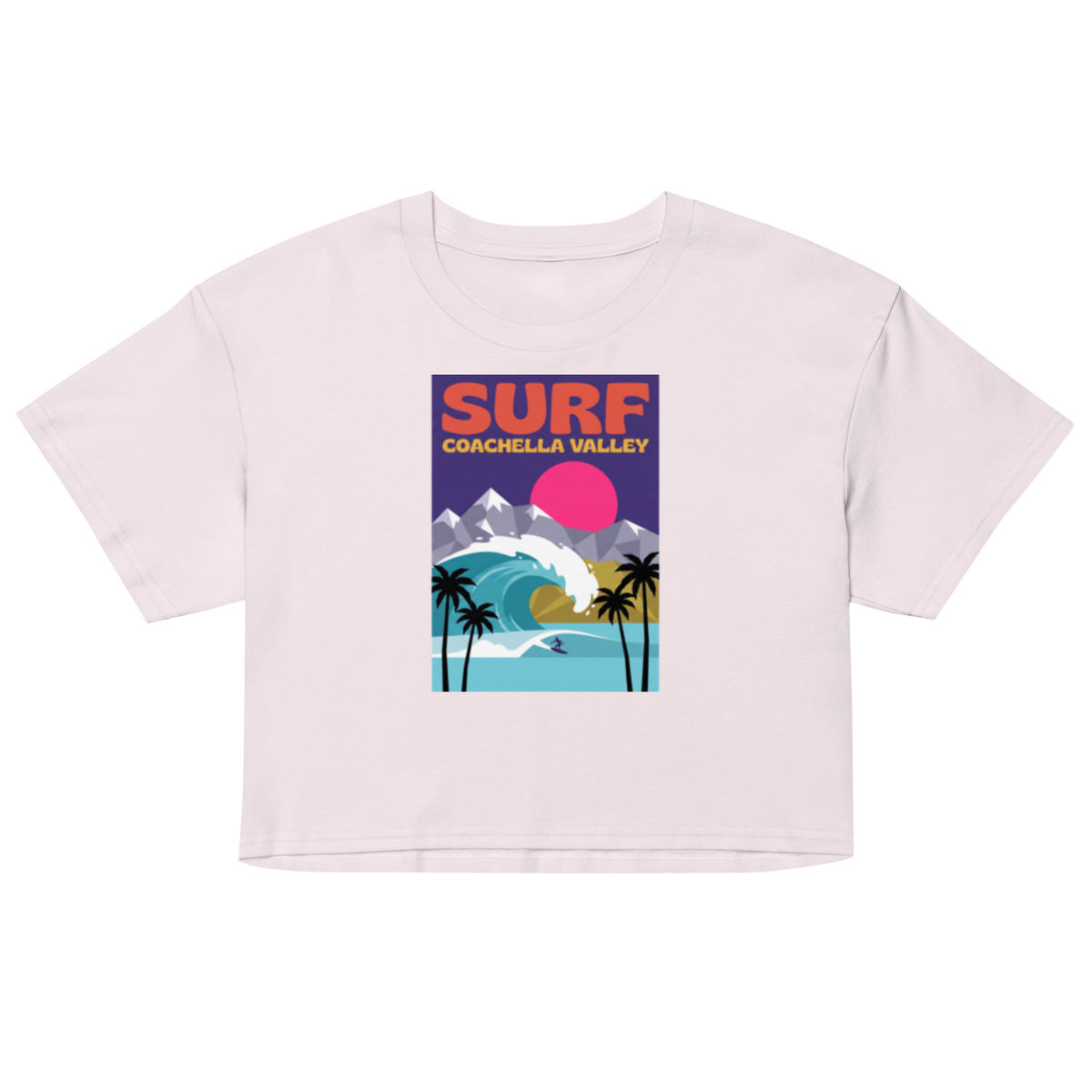 A light pink short-sleeve crop top t-shirt featuring a colorful retro-style graphic on the chest that reads 'SURF COACHELLA VALLEY' above an illustration of palm trees, a wave, mountains, and a pink sun.