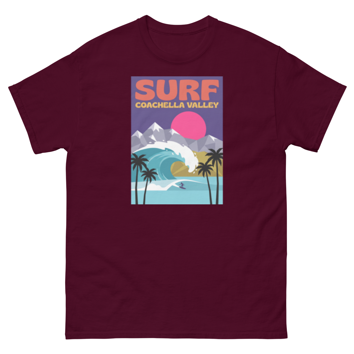 A maroon short-sleeve crewneck t-shirt featuring a colorful retro-style graphic print on the front with the text 'SURF COACHELLA VALLEY' and an illustration of a wave, mountains, palm trees, and a pink sun.