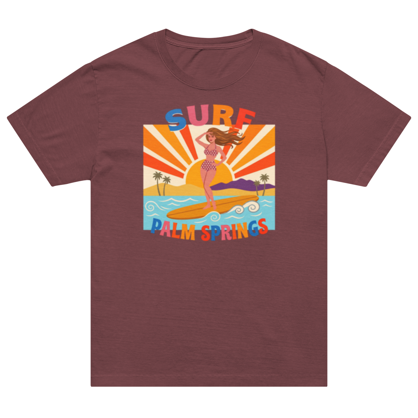A short-sleeve crewneck t-shirt in a dusty rose or mauve color, featuring a colorful retro graphic of a woman surfing on a beach with the text 'SURF PALM SPRINGS'.