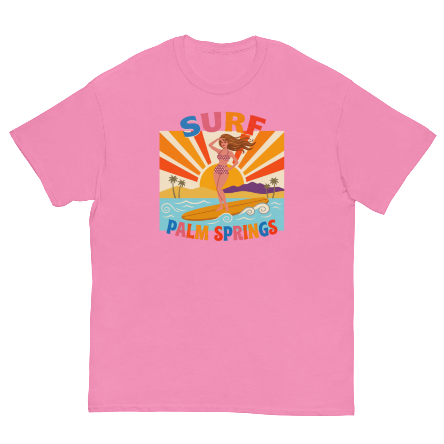 A pink short-sleeve crewneck t-shirt featuring a retro-style graphic of a woman surfing on a yellow board with palm trees and the text 'SURF PALM SPRINGS' in colorful letters.
