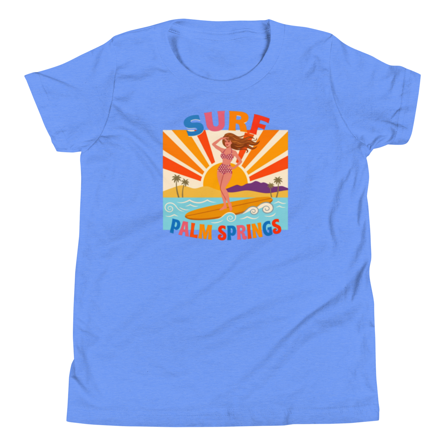 A light blue short-sleeve crewneck t-shirt featuring a colorful retro graphic of a woman surfing on a beach with the text 'SURF PALM SPRINGS'.