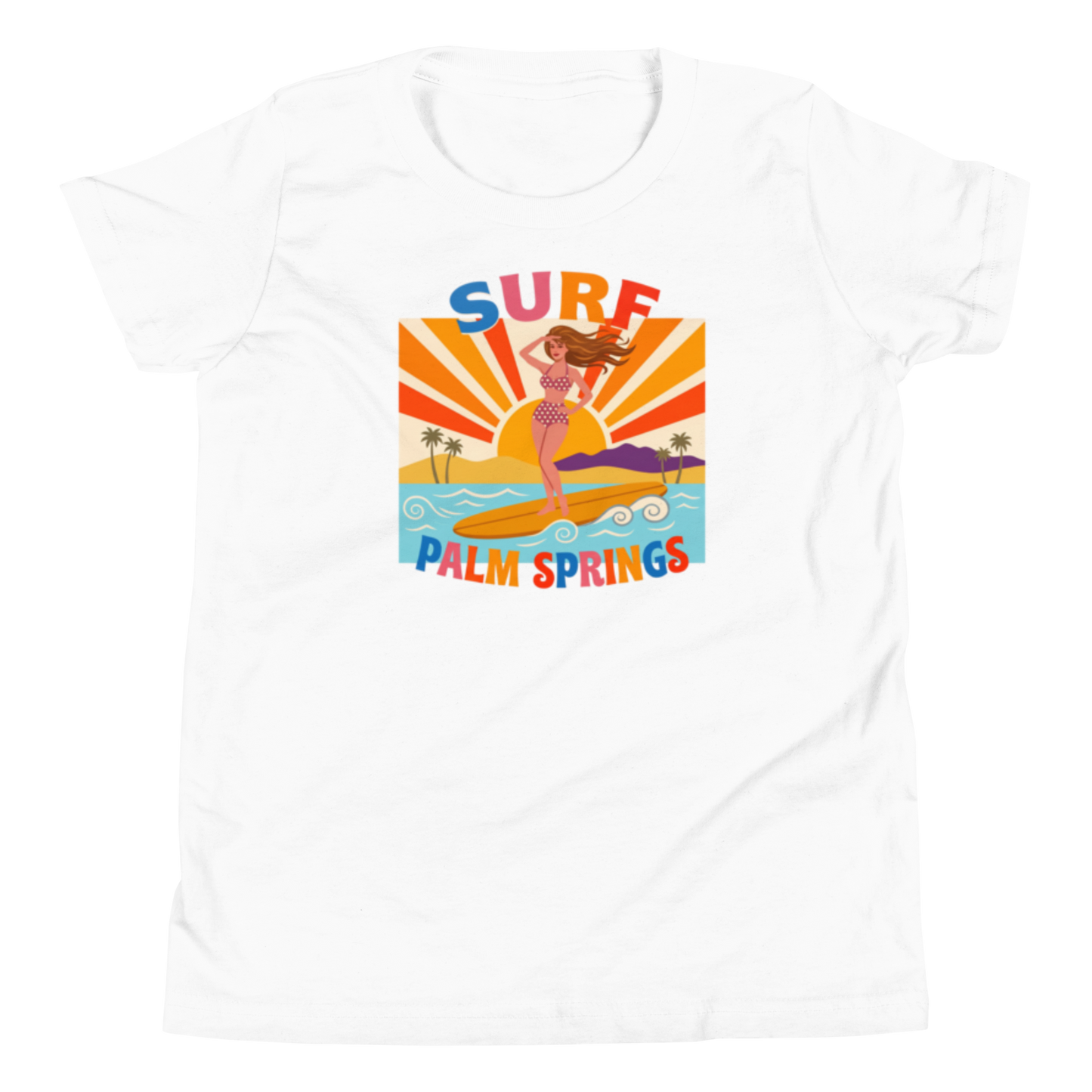 A white short-sleeve crewneck t-shirt featuring a colorful retro graphic of a woman surfing on a beach with the text 'SURF PALM SPRINGS' in stylized lettering.