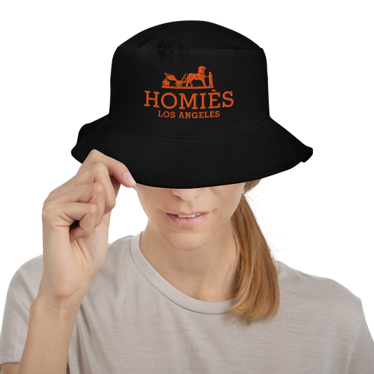 Person wearing a black bucket hat with an embroidered design of a horse and buggy that has text 'Homies Los Angeles'