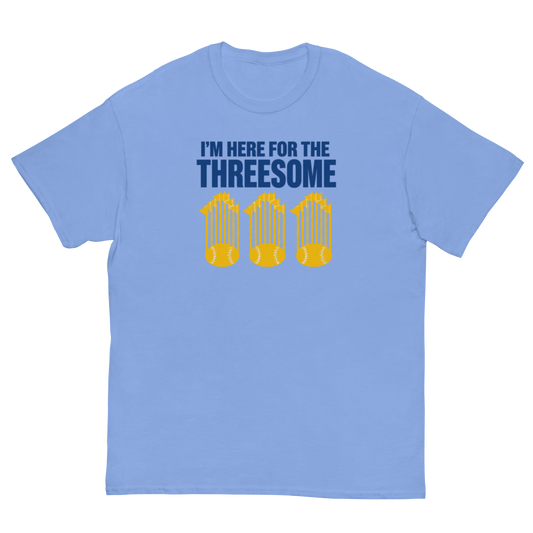 A light blue short-sleeve crewneck t-shirt with a graphic on the chest that reads 'I'M HERE FOR THE THREESOME' in dark blue text above three yellow baseball bats.