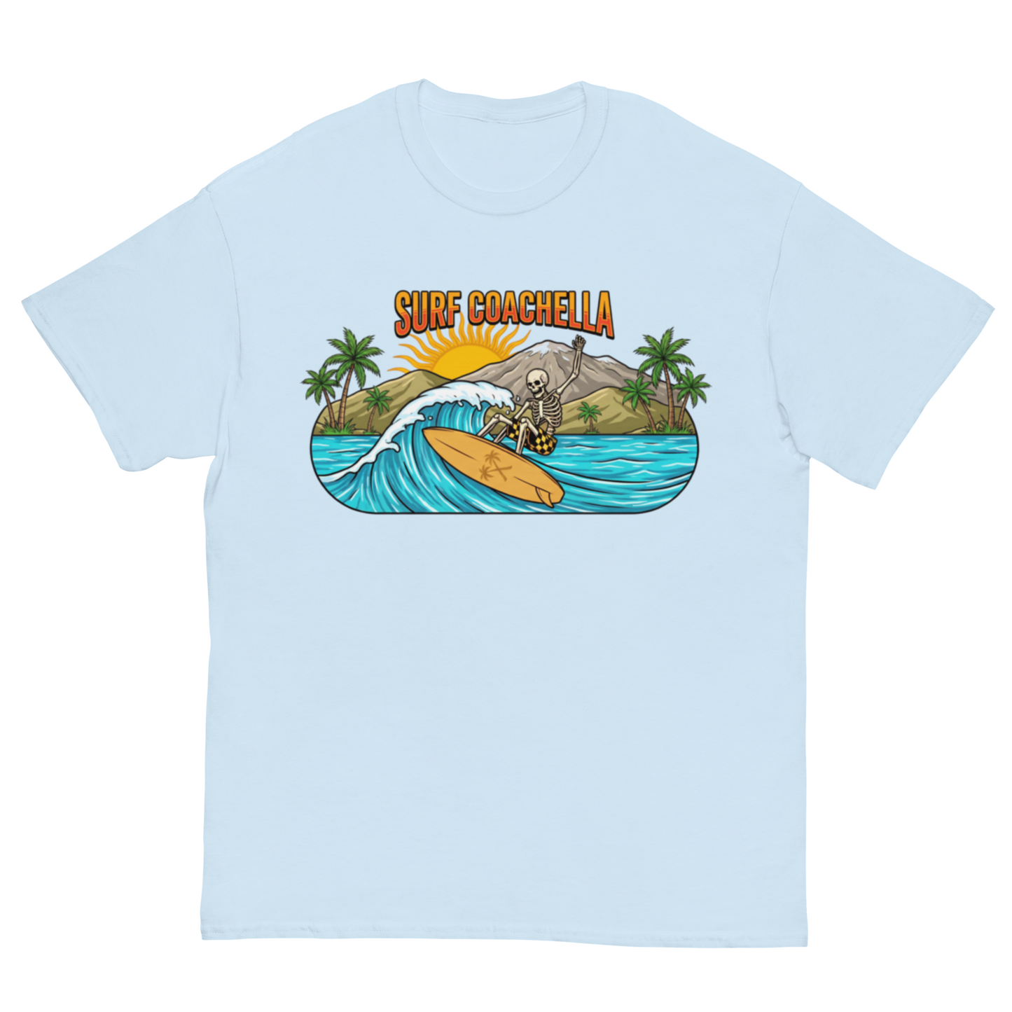 A light blue short-sleeve crewneck t-shirt featuring a colorful graphic print on the front. The graphic shows a skeleton surfer riding a wave on a yellow surfboard, with palm trees, mountains, a rising sun, and the text 'SURF COACHELLA' above.