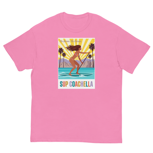 A pink short-sleeve crewneck t-shirt featuring a colorful graphic print on the front. The graphic shows a woman paddleboarding on turquoise water with palm trees and a yellow sunburst background, with the text 'My Dream Surf Spot' and 'SUP COACHELLA' below.