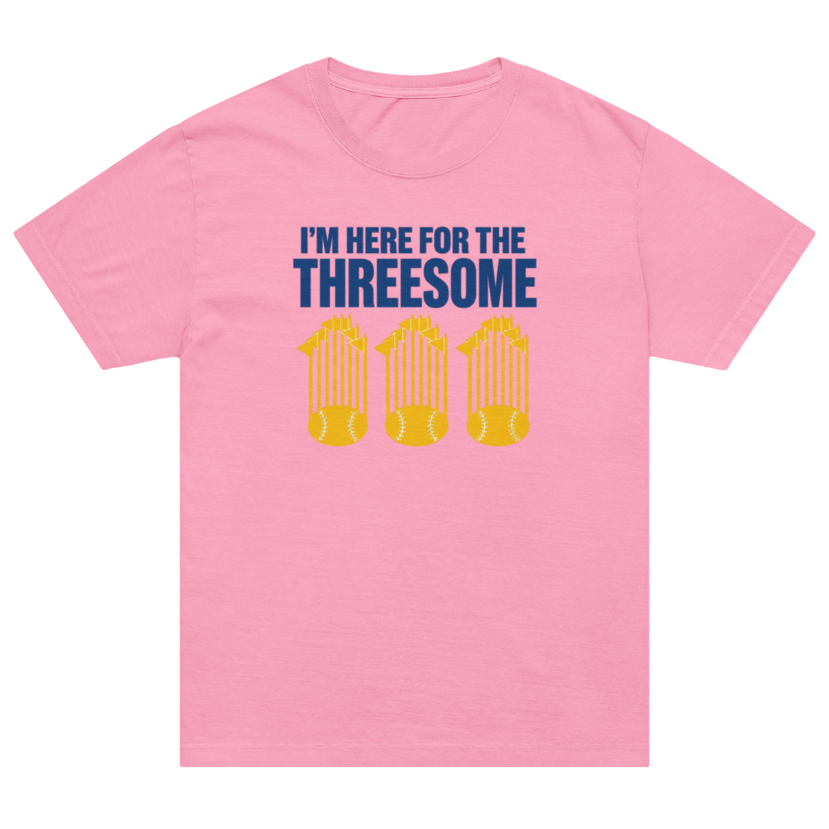 A pink short-sleeve crewneck t-shirt featuring a graphic print on the front. The graphic reads 'I'M HERE FOR THE THREESOME' in dark blue text above three yellow baseballs with trophy crowns.