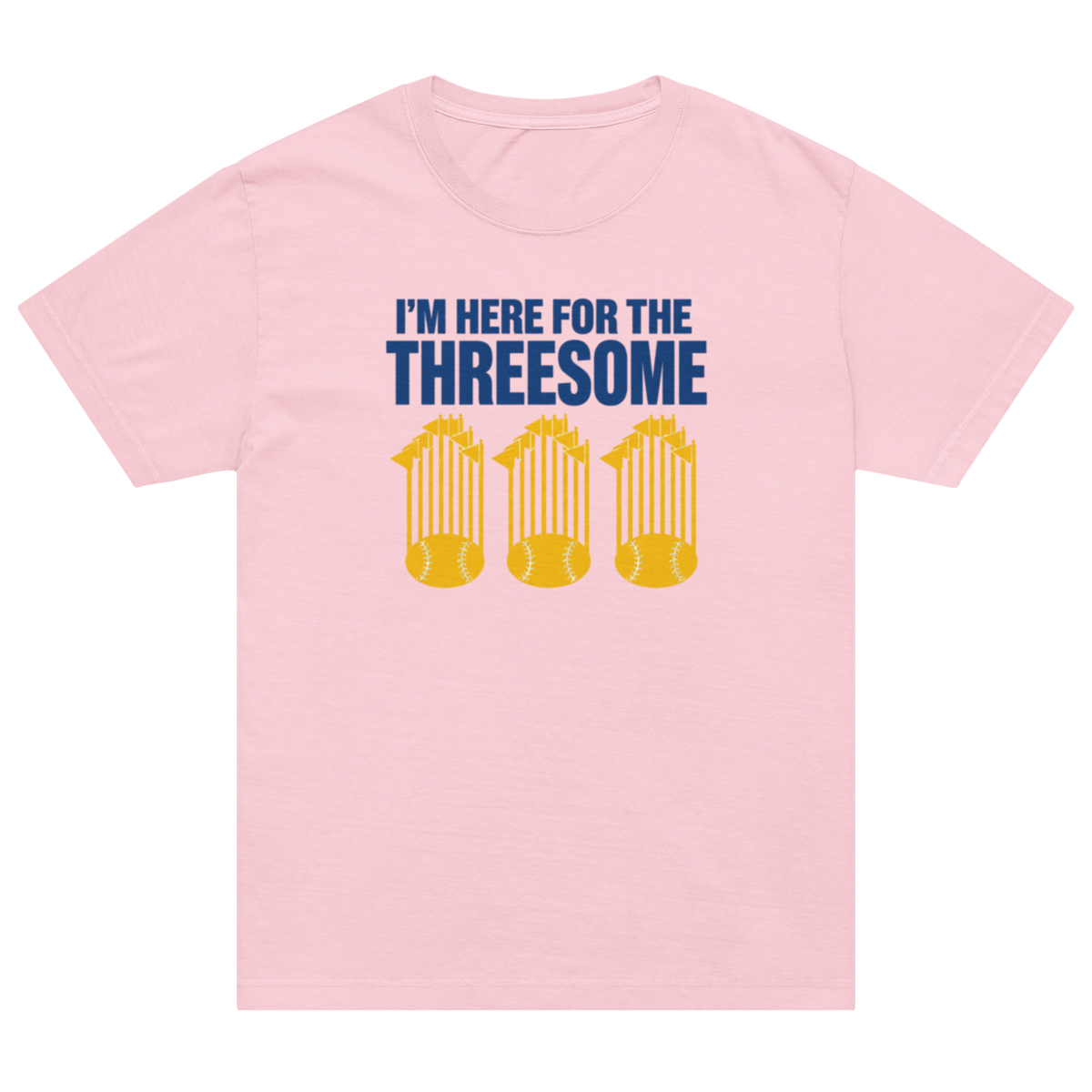 A light pink short-sleeve crewneck t-shirt with a graphic on the front. The graphic features the text 'I'M HERE FOR THE THREESOME' in dark blue, above three yellow silhouettes of baseballs stacked inside trophy cages.