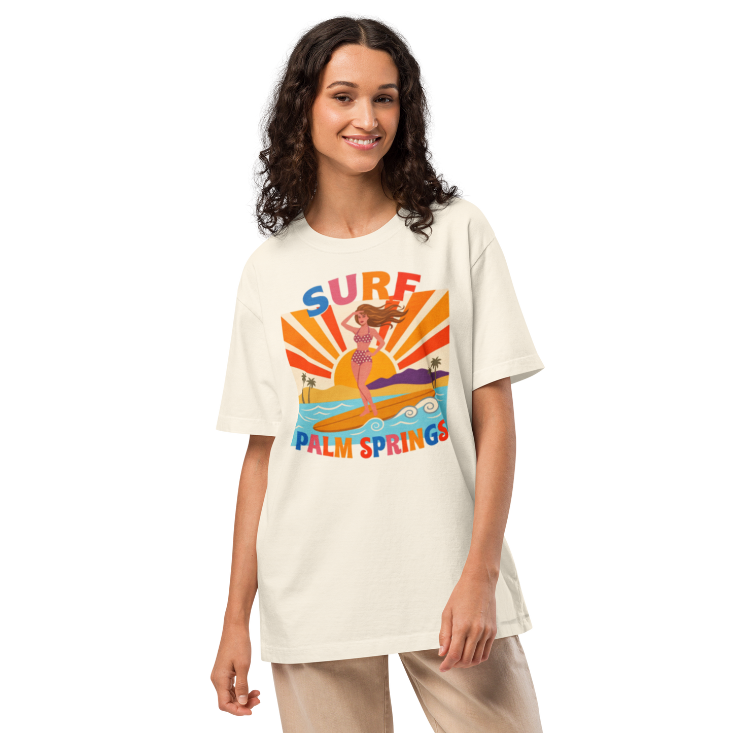 A woman modeling an oversized cream-colored t-shirt with a colorful retro graphic that reads 'SURF PALM SPRINGS' featuring a mermaid and sun rays.