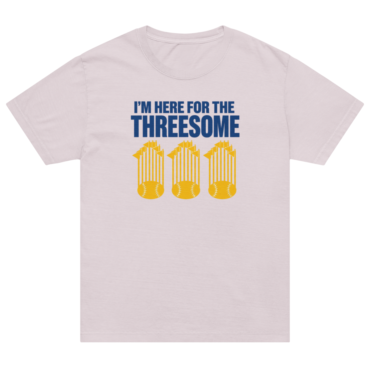 A light pink crewneck t-shirt with a graphic print that reads 'I'M HERE FOR THE THREESOME' in blue, above three yellow baseballs stacked on top of each other.