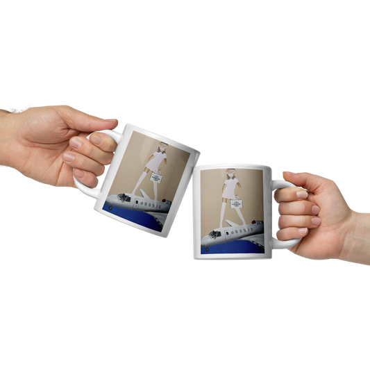 Two hands holding white ceramic mugs with a printed graphic of a woman in a white dress walking on a blue and gray airplane runway. Daniel Maltzman artist.