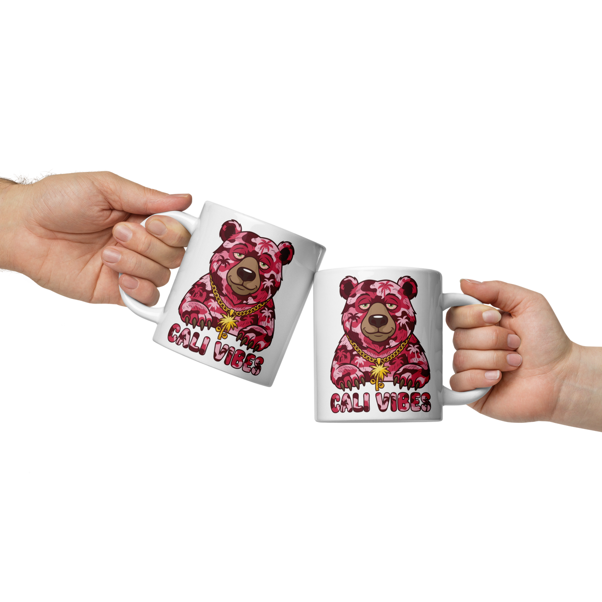 Two white ceramic mugs with a pink camouflage bear graphic and the text 'CALI VIBES' are held by two hands against a white background.