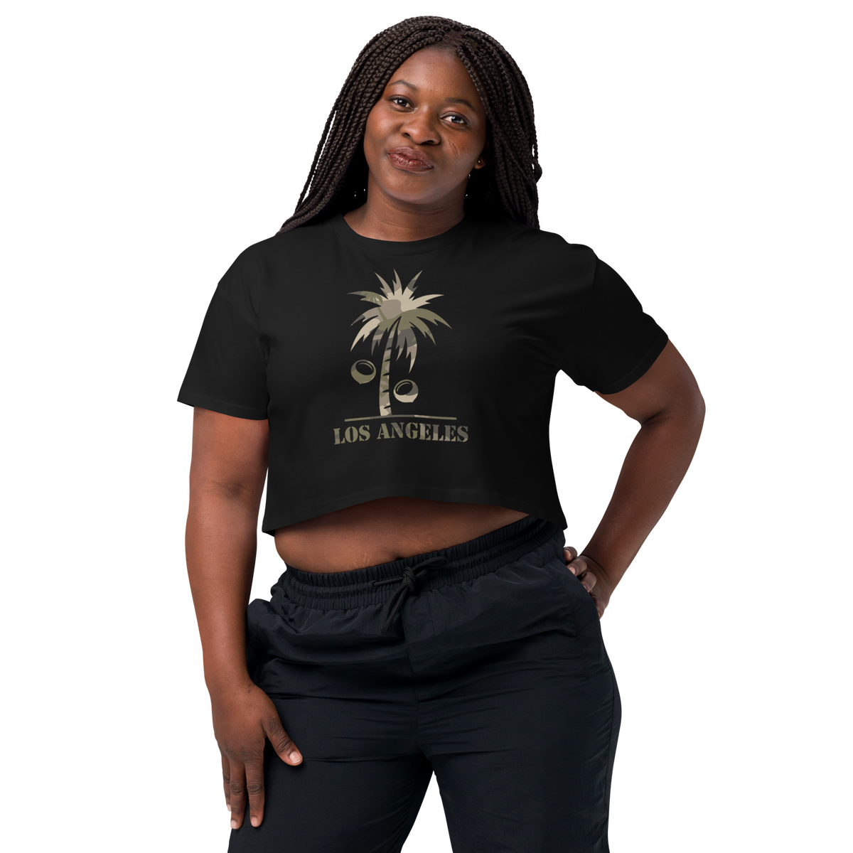 A woman modeling a black cropped t-shirt with a distressed gold palm tree graphic and the text 'LOS ANGELES' underneath, paired with black sweatpants against a solid white background.