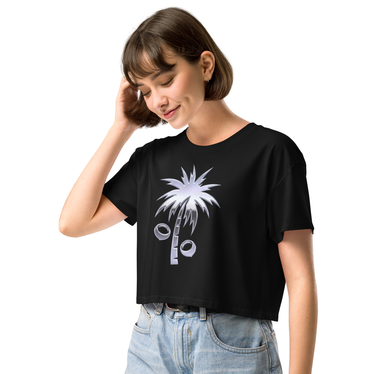 A woman wearing a black short-sleeve crop top t-shirt with a y2k chrome palm tree graphic, paired with light blue jeans, set against a plain white background.