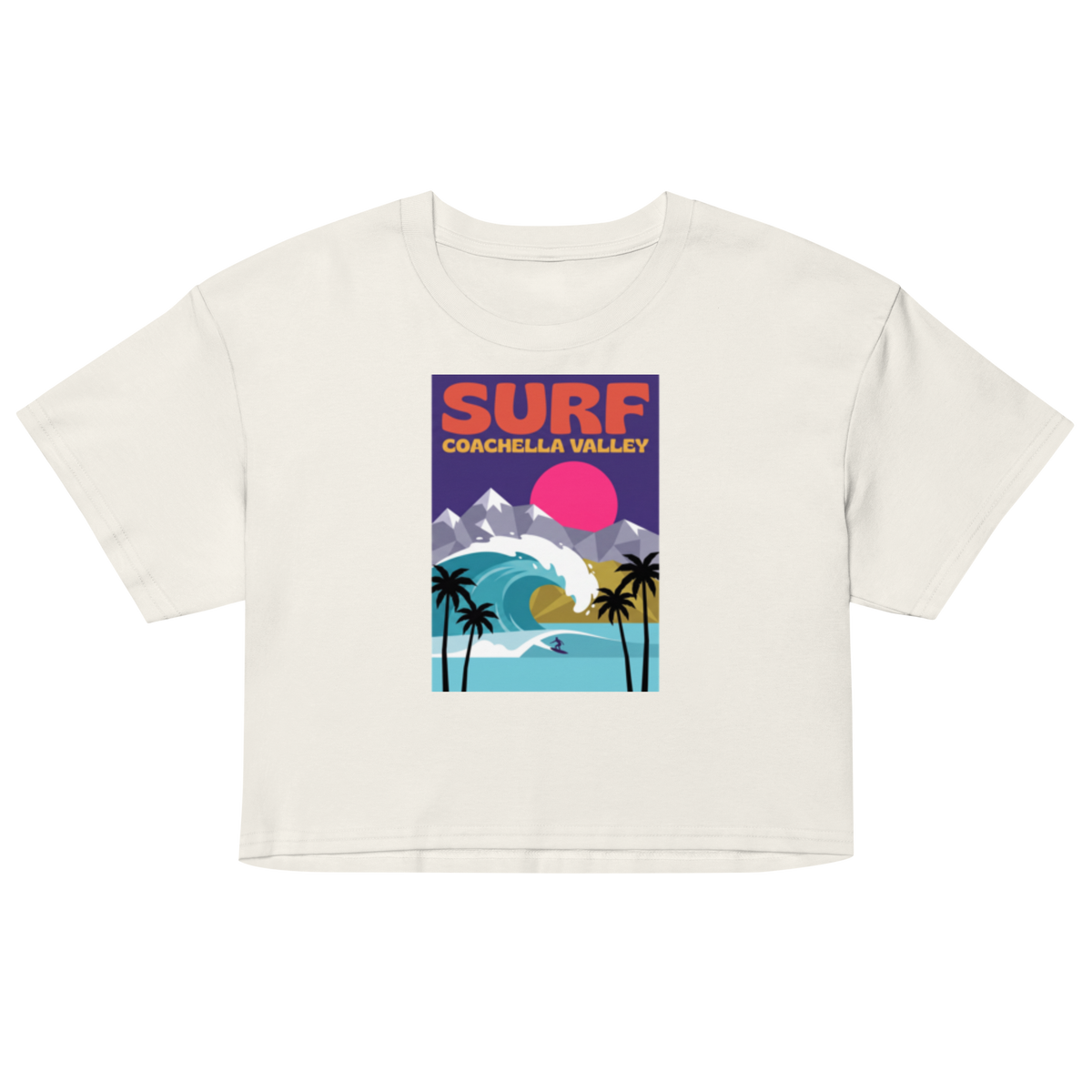 An off-white cropped t-shirt featuring a colorful retro-style graphic print that reads 'SURF COACHELLA VALLEY' above an illustration of palm trees, mountains, a wave, and a pink sun.