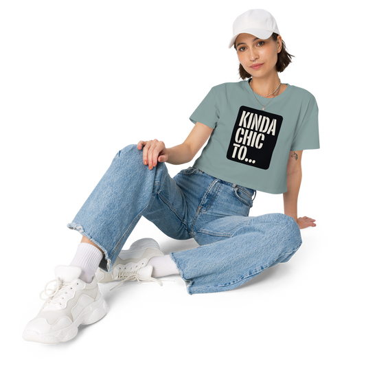 A woman wearing a sage green graphic t-shirt with a black box containing the text 'KINDA CHIC TO.