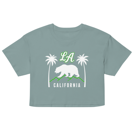A cropped short-sleeve t-shirt in a dusty sage green color, featuring a California-themed graphic on the front with a white bear, green mountains, palm trees, 'LA' in green, and 'CALIFORNIA' in white.