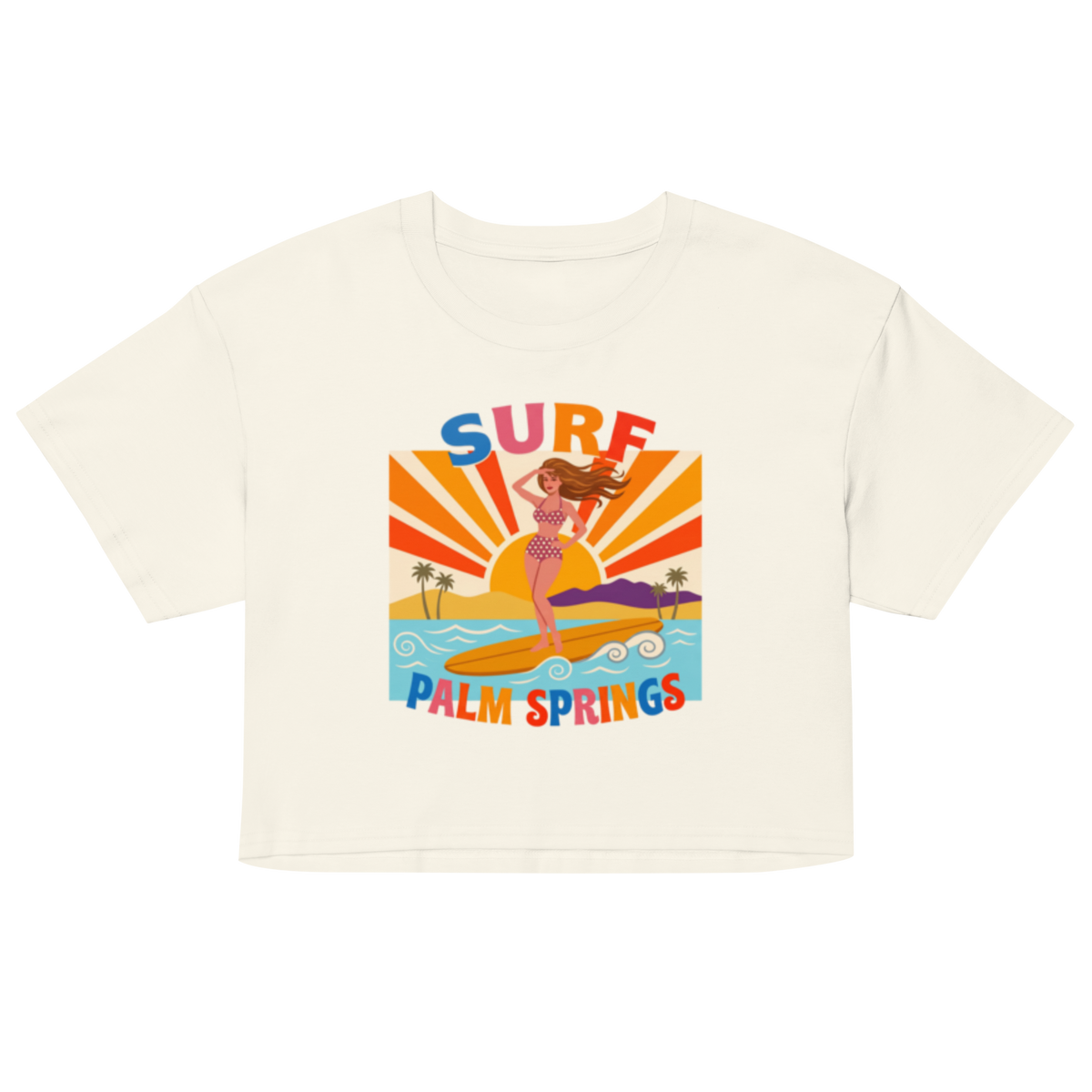 An off-white short-sleeve crop top featuring a colorful retro graphic of a woman surfing on a beach with the text 'SURF' and 'PALM SPRINGS'.
