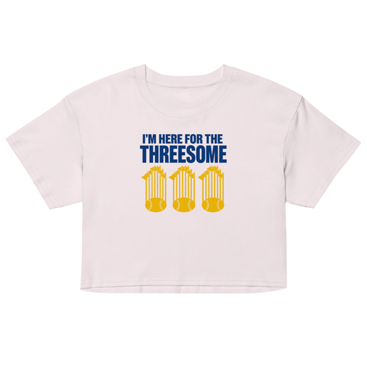 A light pink short-sleeve crop top t-shirt with a graphic print on the front. The graphic features the text 'I'M HERE FOR THE THREESOME' in bold blue letters above three yellow columns of beer glasses.