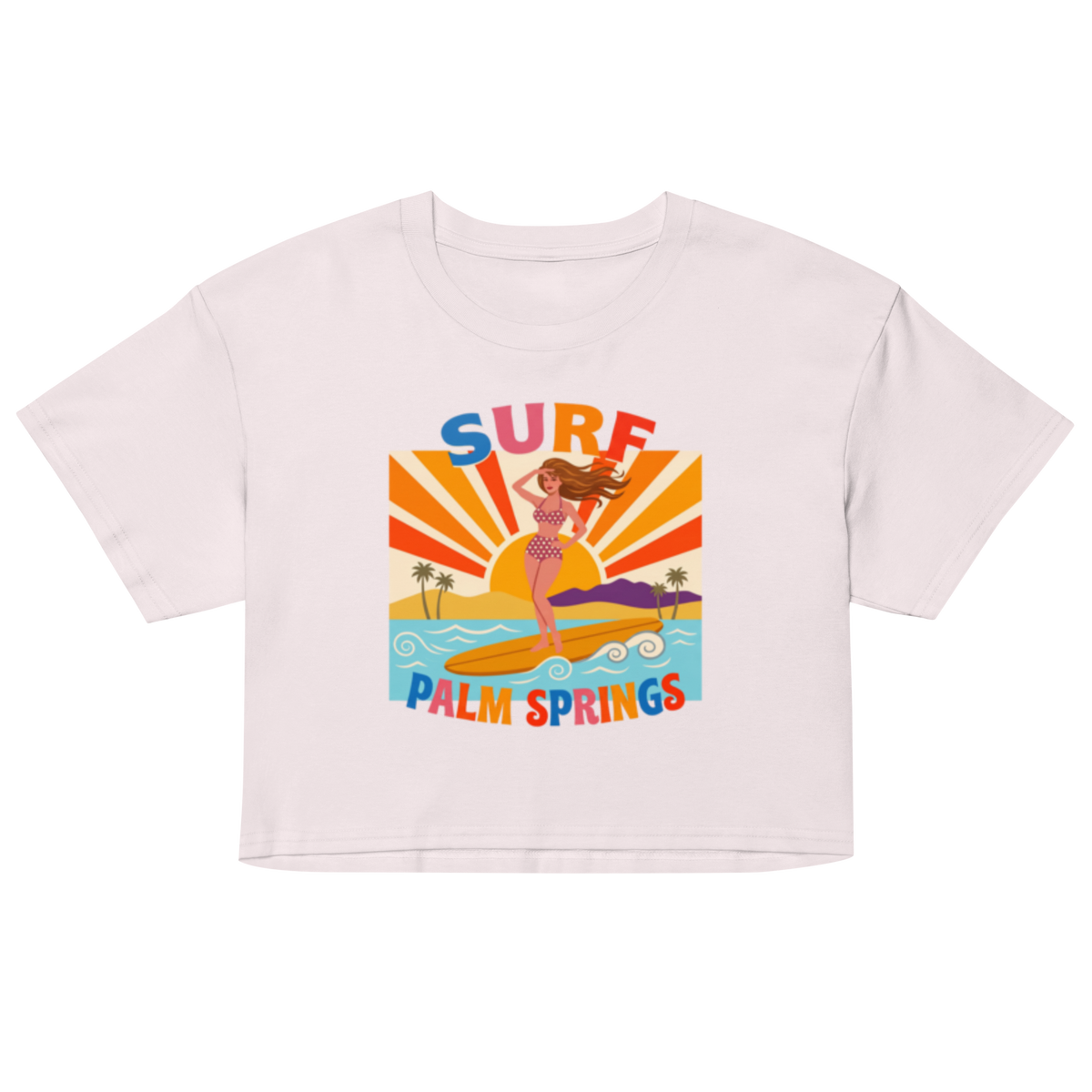A white short-sleeve crop top featuring a colorful retro graphic of a woman surfing on a palm beach with the text 'SURF PALM SPRINGS'.