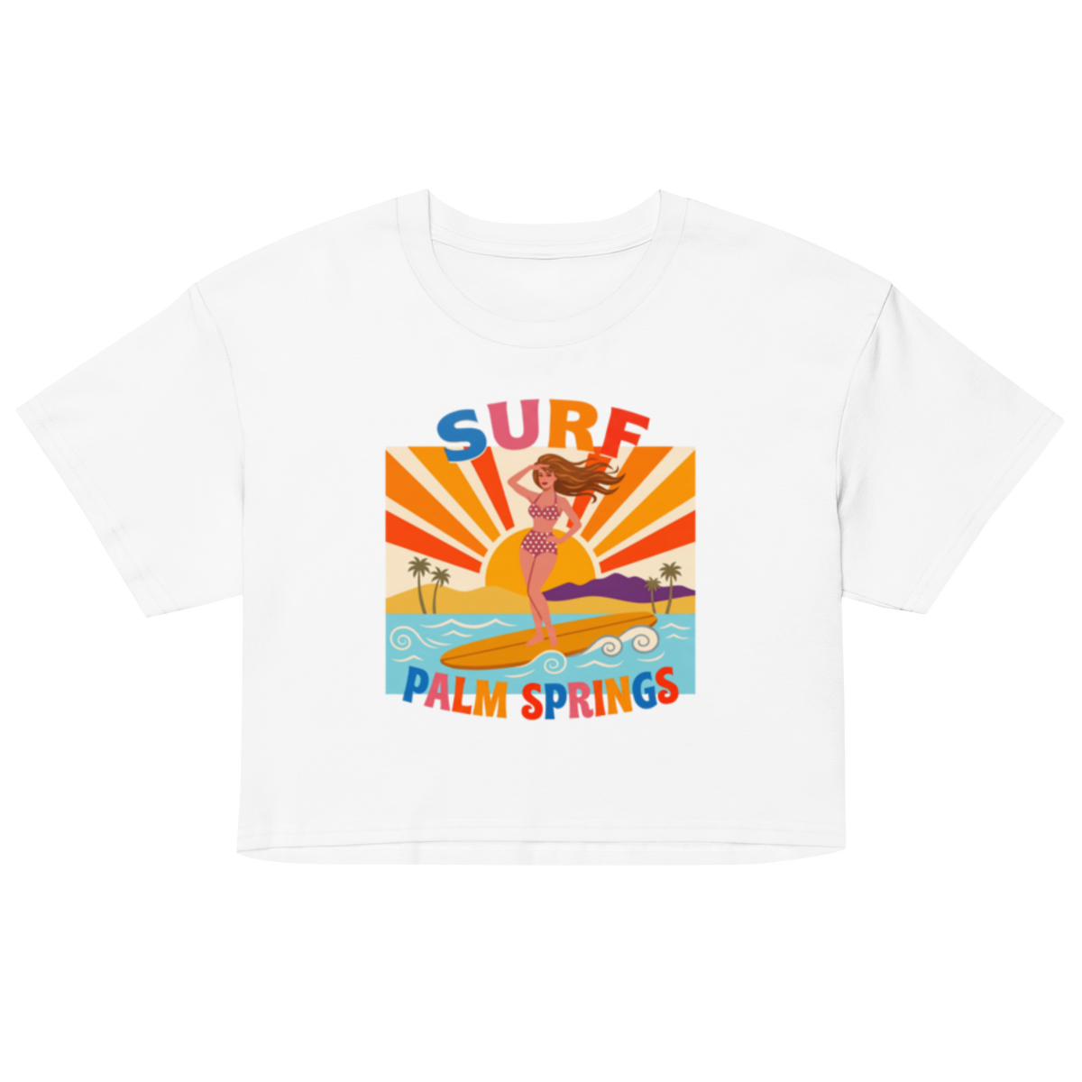A white cropped short-sleeve t-shirt featuring a colorful retro graphic of a woman surfing on a beach with the text 'SURF PALM SPRINGS' in bold multicolor letters.