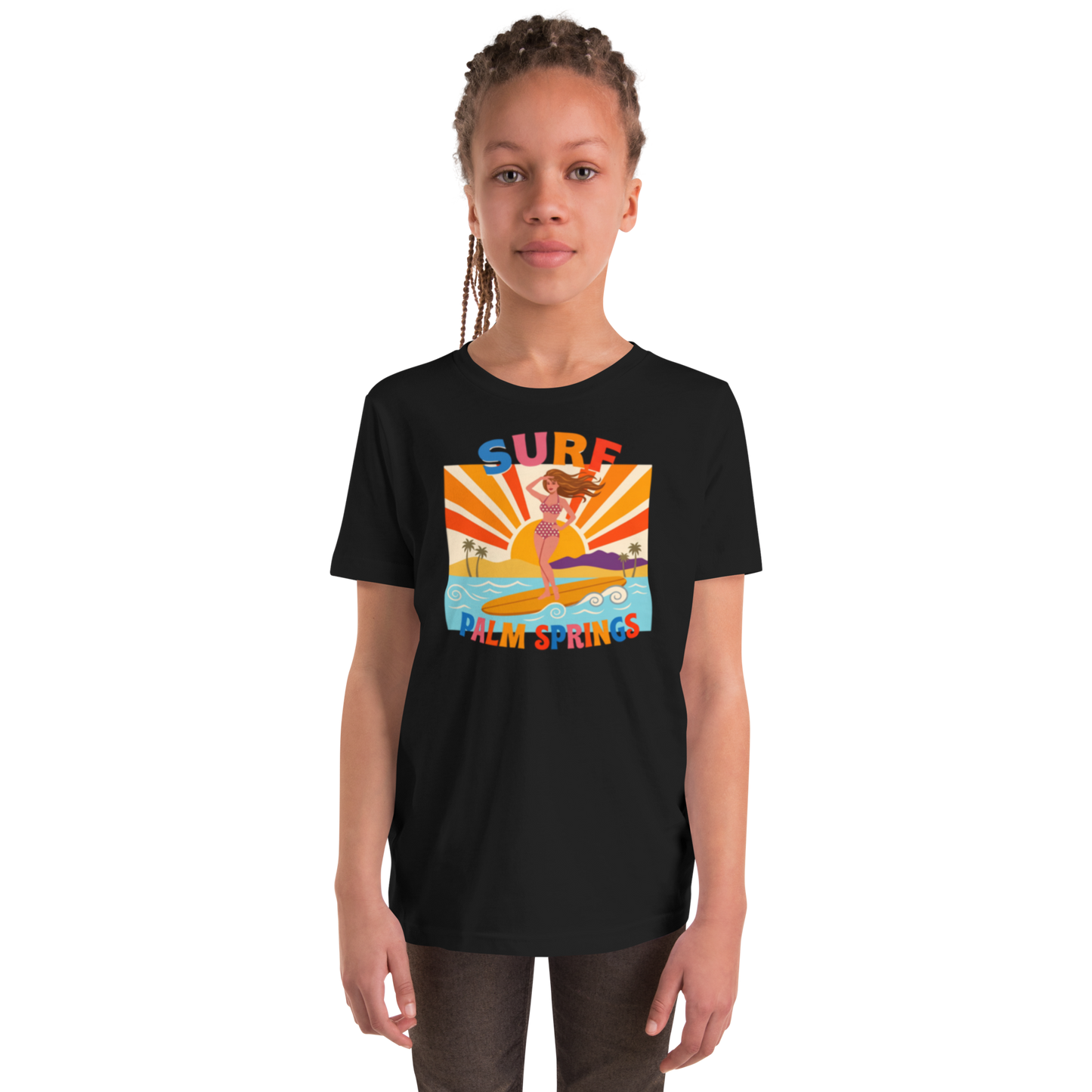 A young girl with braided hair wearing a black short-sleeve t-shirt with a colorful retro graphic that reads 'SURF Palm Springs' and shows a woman in a yellow bikini on a surfboard. The photo is shot against a clean white background.
