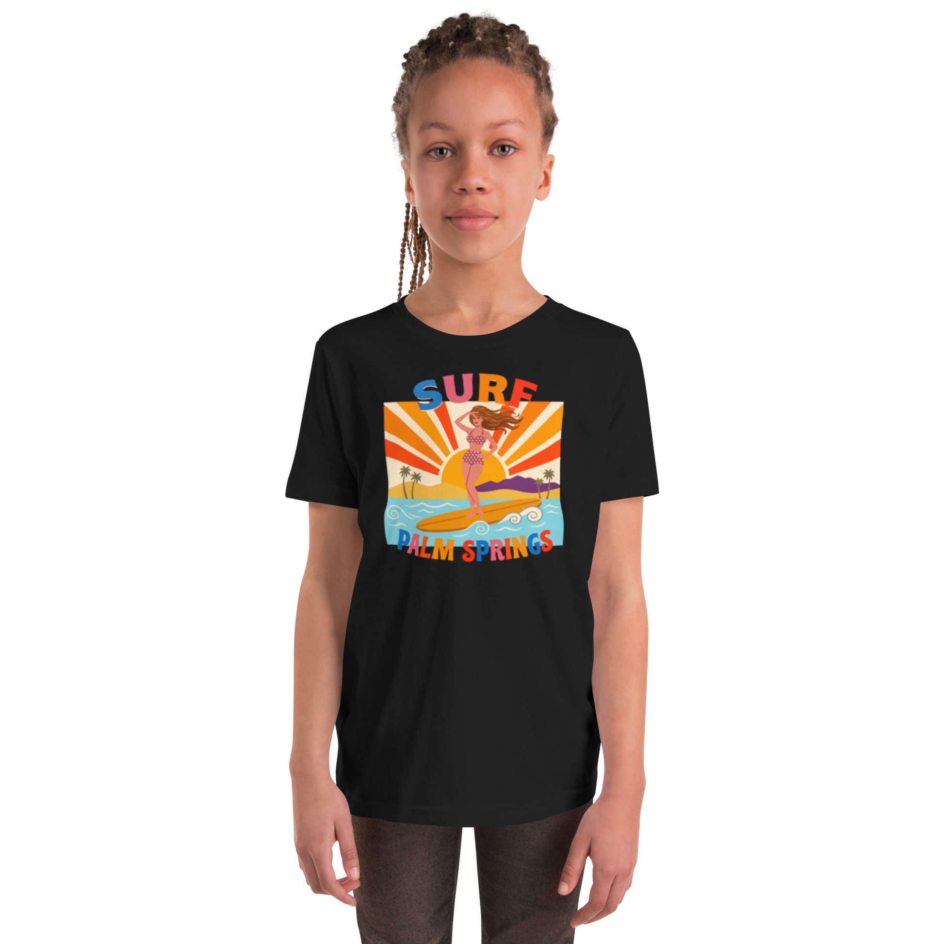 A young girl with braided hair wearing a black short-sleeve t-shirt with a colorful retro graphic that reads 'SURF Palm Springs' and shows a woman in a yellow bikini on a surfboard. The photo is shot against a clean white background.