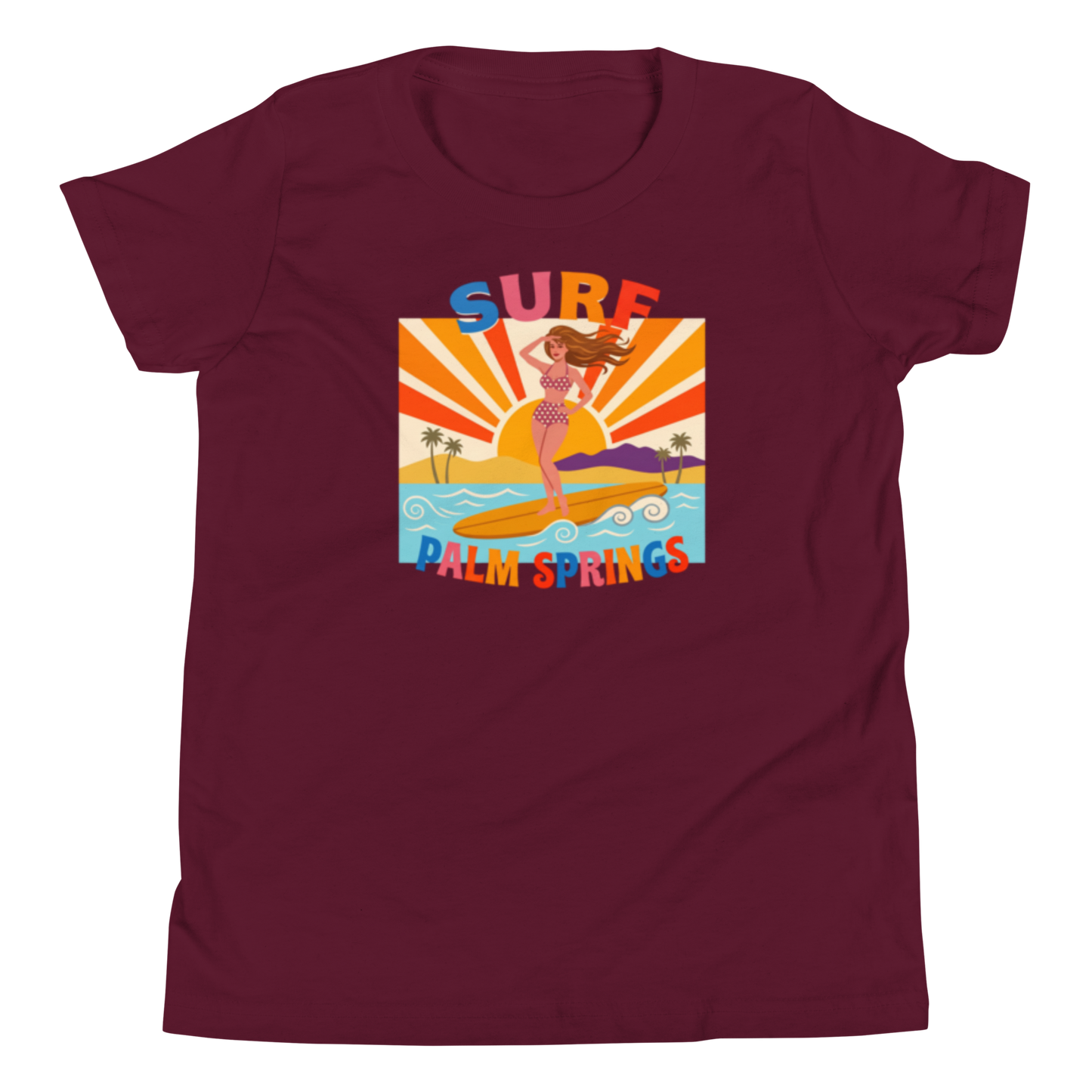 A maroon short-sleeve crewneck t-shirt featuring a colorful retro graphic of a mermaid surfing on a beach with the text 'SURF PALM SPRINGS'.