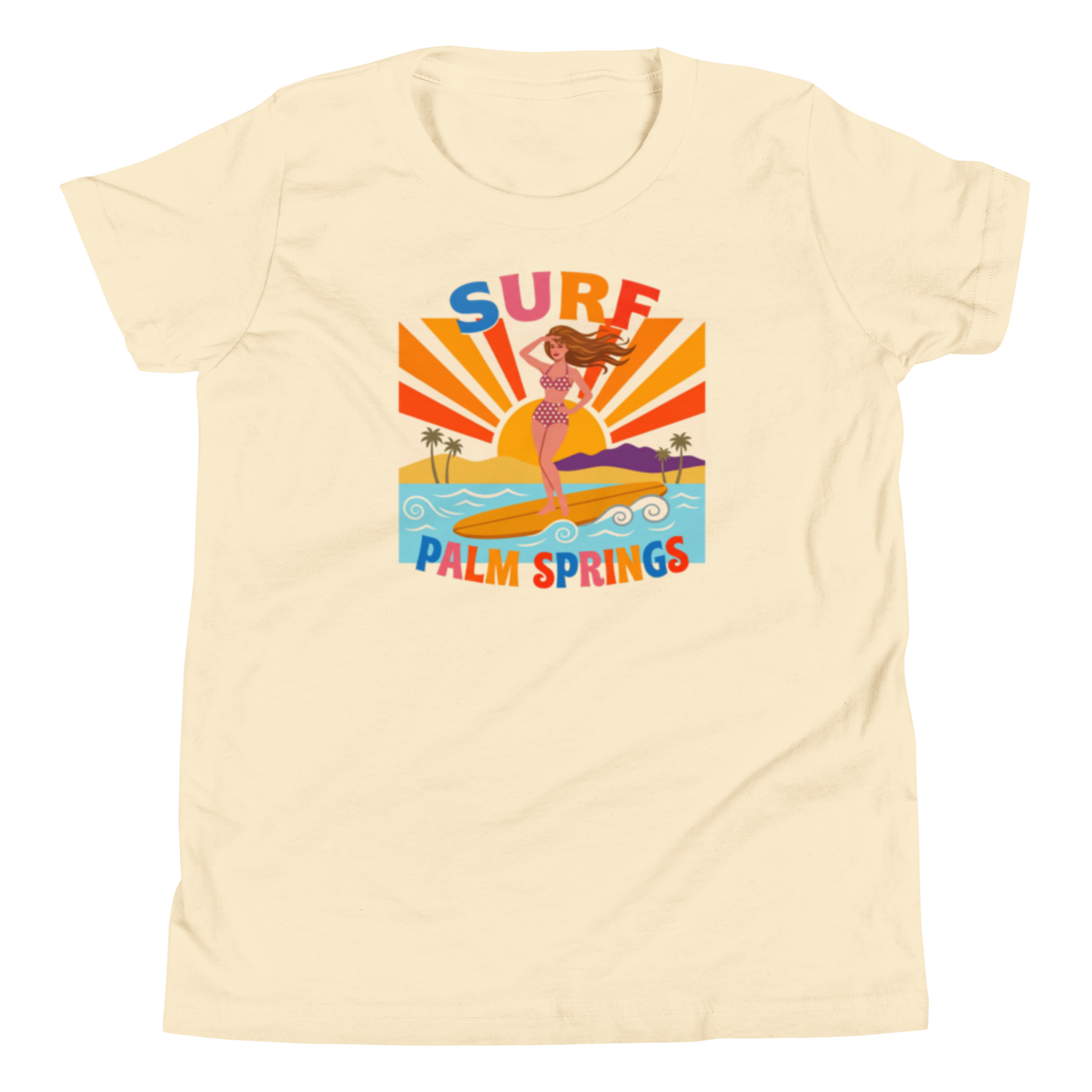 A cream-colored short-sleeve t-shirt with a colorful retro graphic of a mermaid surfing on a beach with the text 'SURF PALM SPRINGS'.